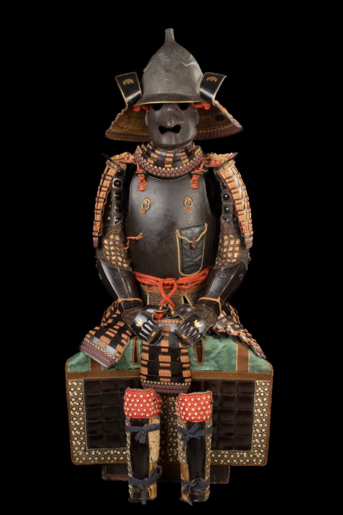 Japanische Samurai-Rüstung des Feudalherrn Satake Yoshizumi mit einem glatten, rotbraunen Eisenbrustpanzer, gruppierter Schnürung, schwarz lackierten Karuta-Oberschenkelschützern und Schienbeinschonern mit sechseckigen Kikkō-Verstärkungen.