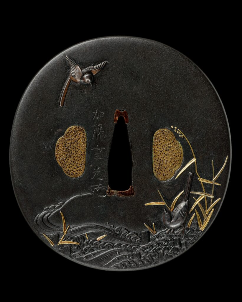 Japanisches Schwertstichblatt (Tsuba) aus Eisen von Katō Shigemitsu (1747–1824) mit Vögeln und Schilf am Ufer eines Gewässers sowie geflochtenen Schanzkörben zur Uferbefestigung. Aus der Sammlung des Samurai Museum Berlin.