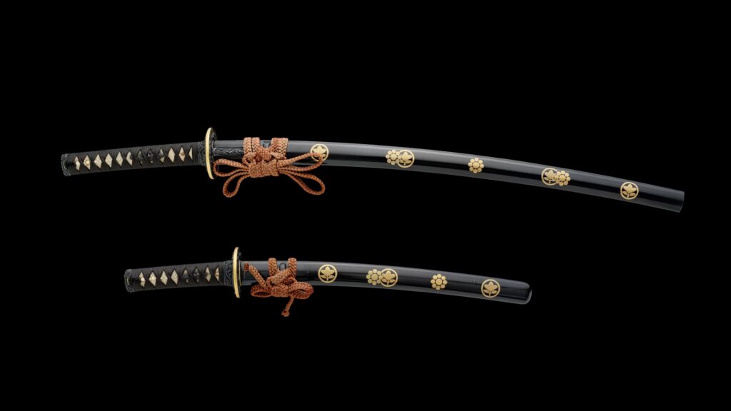 A pair of daishō sword mountings for a katana and wakizashi, featuring black lacquered, mirror-polished scabbards with gold-decorated family crests of the Ii and Kikkawa clans. Signed by Ōmori Teruhide (1730–1798). 