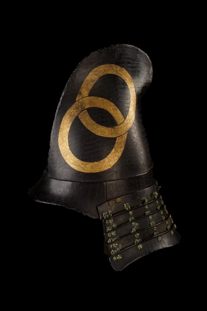 Japanese samurai helmet shaped like an eboshi cap, featuring black lacquer and a wave pattern, a golden wachigai family crest, a five-tier neck guard (hineno jikoro) and a V-shaped face mask (tsubame bō) with a throat guard.