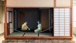 Zwei Personen in traditioneller japanischer Kleidung vollziehen eine Teezeremonie in einem Tatami-Raum mit Shoji-Schirmen und Holzrahmen.
